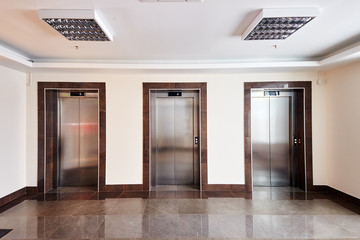 Modern minimalist business centre lobby interior with three closed steel lift doors