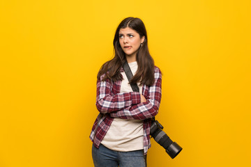 Photographer teenager girl over yellow wall with confuse face expression while bites lip