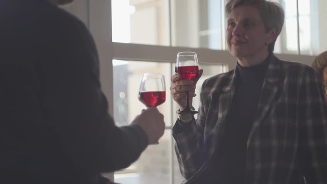 Back of man with glass of red wine and portrait of happy senior woman with grey short hair with glass of wine. Couple talk and enjoy time together. Family relationships.