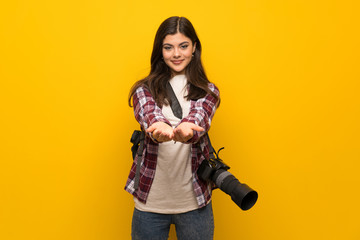 Fototapeta na wymiar Photographer teenager girl over yellow wall holding copyspace imaginary on the palm to insert an ad
