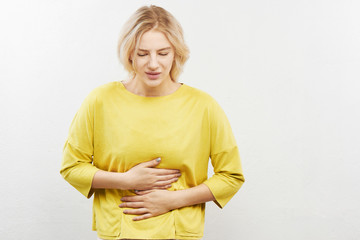 Woman with suffer expression on face holding stomach and squirming with pain. Indigestion,...