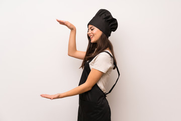 Teenager chef  over white wall holding copyspace to insert an ad
