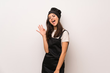 Naklejka premium Teenager chef over white wall saluting with hand with happy expression