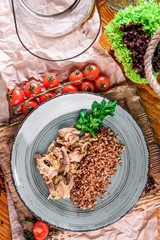 buckwheat with stewed mushrooms in a gray plate on a wooden board in a rustic composition. close-up. top view. flat lay
