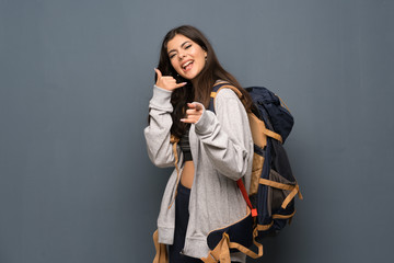 Teenager traveler girl over wall making phone gesture and pointing front