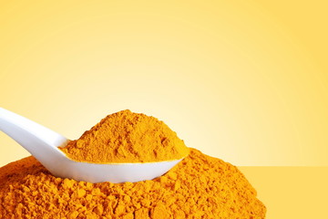 turmeric or curcumin longa root powder in spoon  isolated on yellow background