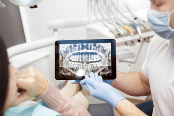 Discussing issues. Cropped shot of a professional dentist showing jaws and teeth x-rays to his patient using a digital tablet technology gadget online issues healthcare medical profession help concept