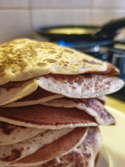 A stack of Russian pancakes close-up on a blurred background with a frying pan on a gas stove