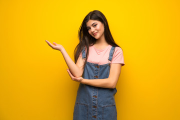 Teenager girl over yellow wall extending hands to the side for inviting to come