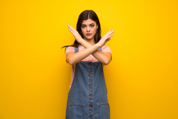 Teenager girl over yellow wall making NO gesture