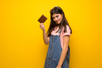 Teenager girl over yellow wall holding a wallet