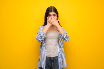 Teenager girl over yellow wall covering mouth with hands for saying something inappropriate