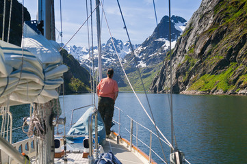 young woman on lookout at the bow of a sailing yacht, entering the famous Troll Fjord in the Lofoten Islands, northern Norway