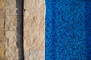 Blue ripped water in swimming pool in tropical resort with edge of pavement. Part of Swimming pool bottom background. Clear light blue pool water ripples with sun reflection. Surface of swimming pool.