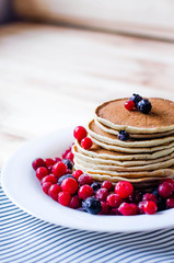 A stack of pancakes with blueberries and cranberries on a white plate.