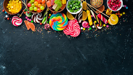 Colorful candies and lollipops. On a black stone background. Top view. free copying space.