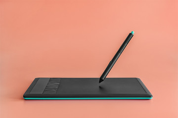 Black and blue graphics tablet and levitating stylus on light pink color background.