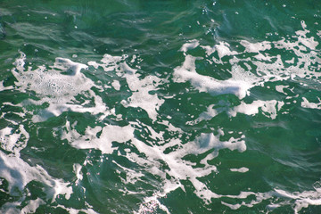 Turquoise green seawater with sea foam as background, close up. Surface of sea with waves, splash, foam and bubbles, blue abstract texture and wallpaper. Beautiful green waves with a lot of sea foam.