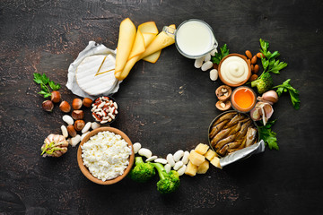 Group of products rich in calcium. Healthy diet food: cheese, milk, parmesan, sour cream, fish, almonds, parsley, garlic, broccoli. On the old background. Top view. Free copy space.