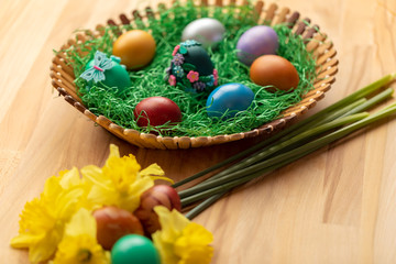 Basket full of colorful easter eggs with flowers by side