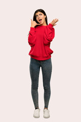 A full-length shot of a Teenager girl with red sweater making phone gesture and doubting over isolated background