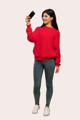 A full-length shot of a Teenager girl with red sweater making a selfie over isolated background