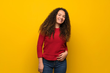 Teenager girl with red sweater over yellow wall laughing looking to the front