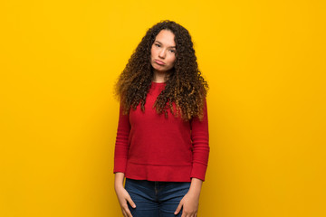 Teenager girl with red sweater over yellow wall with sad and depressed expression