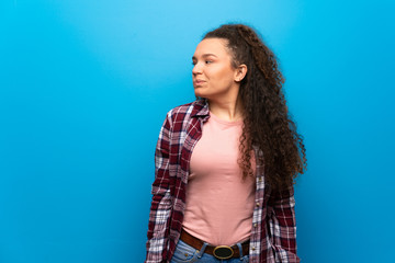 Teenager girl over blue wall making unimportant gesture