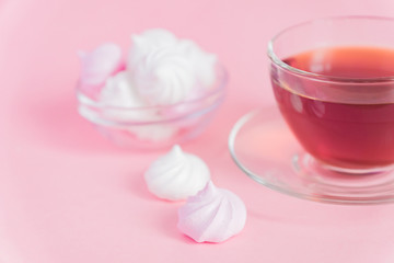 Obraz na płótnie Canvas White and pink twisted meringues and cup of tea on pink background. French dessert prepared from whipped with sugar and baked egg whites. Greeting card with copy space