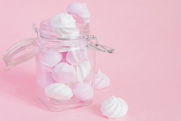 White and pink twisted meringues in a glass jar on pink background. French dessert prepared from whipped with sugar and baked egg whites. Greeting card with copy space
