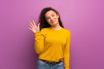 Teenager girl over purple wall counting five with fingers