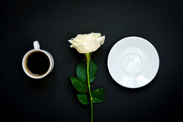 Cup of black coffee and white rose on black background, Top view, copy space.