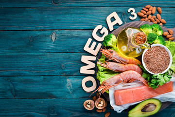 Foods containing omega 3. Vitamin Healthy foods: avocados, fish, shrimp, broccoli, flax, nuts, eggs, parsley. Top view. Free space for your text. On a blue wooden background. - obrazy, fototapety, plakaty