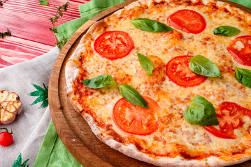 tasty traditional margarita pizza on a round wooden board on a red wooden background, decorated with napkins, chili pepper and cherry tomatoes. close-up. for menu