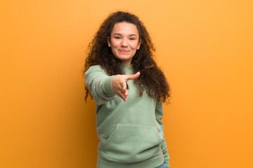 Teenager girl over ocher wall shaking hands for closing a good deal