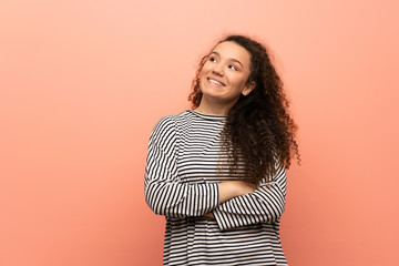 Teenager girl over pink wall looking up while smiling