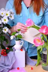 Woman wearing a blue blouse is composing a bouquet of tulips and chrysanthemums and puts a card into the envelope