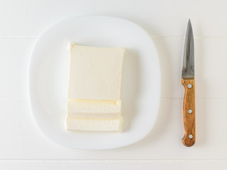 Knife and Serbian cheese on a white bowl on a white table. The view from the top. Dairy product.