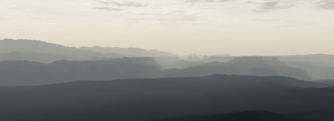 Mountain range in mist under cloudy sky.