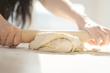 Woman rolls out the dough on the table with a rolling pin, female hands soiled in flour close-up. Concept of baker, cooking, housewife, baking of pie or pizza