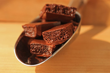 Milk porous chocolate in a steel scoop on a wooden background