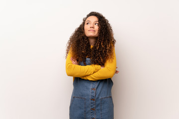 Teenager girl with red sweater over white wall making doubts gesture while lifting the shoulders