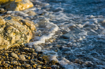 pebble stones on the sea beach, the rolling waves of the sea with foam