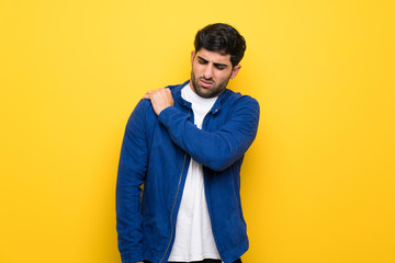 Man with blue jacket over yellow wall suffering from pain in shoulder for having made an effort