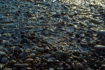 pebble stones on the sea beach, the rolling waves of the sea with foam