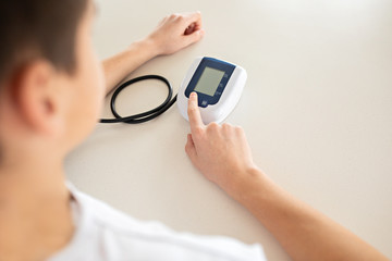 Hypertension concept. Teenager is measuring blood pressure with monitor in home. Hands close-up