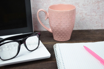 Computer image coffee cup resting on a wooden backgroud. desktop, work space of a journalist, blogger, freelancer, office supplies glasses pen, notebook