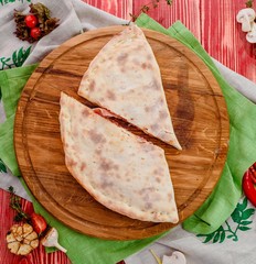 Half of the baked calzone - closed type of pizza that is folded in half, on a round wooden board on...