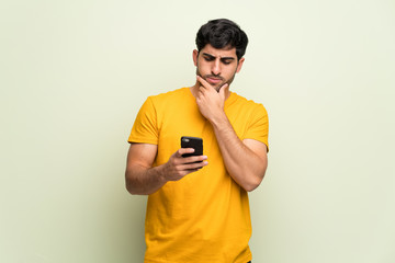 Young man over pink wall celebrating a victory with a mobile